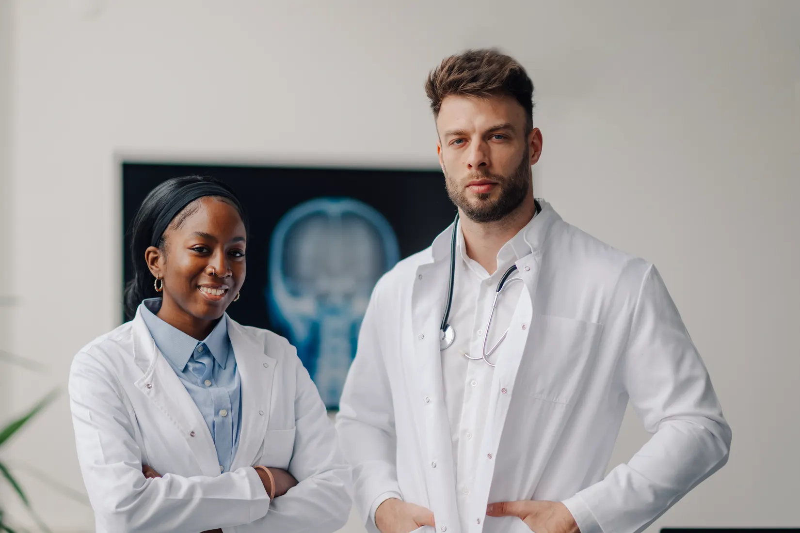 Two clinicians in white coats standing in a clinic in front of an X-ray display.