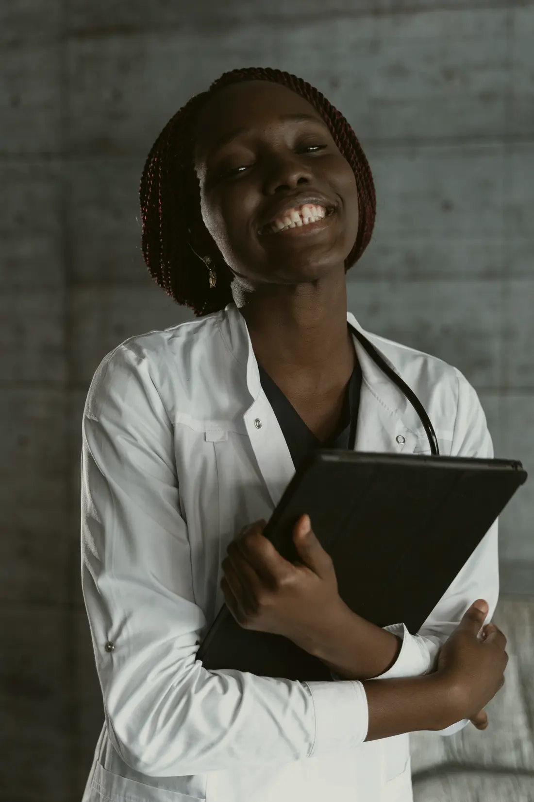 A smiling clinician in a white coat and stethoscope, holding a tablet.